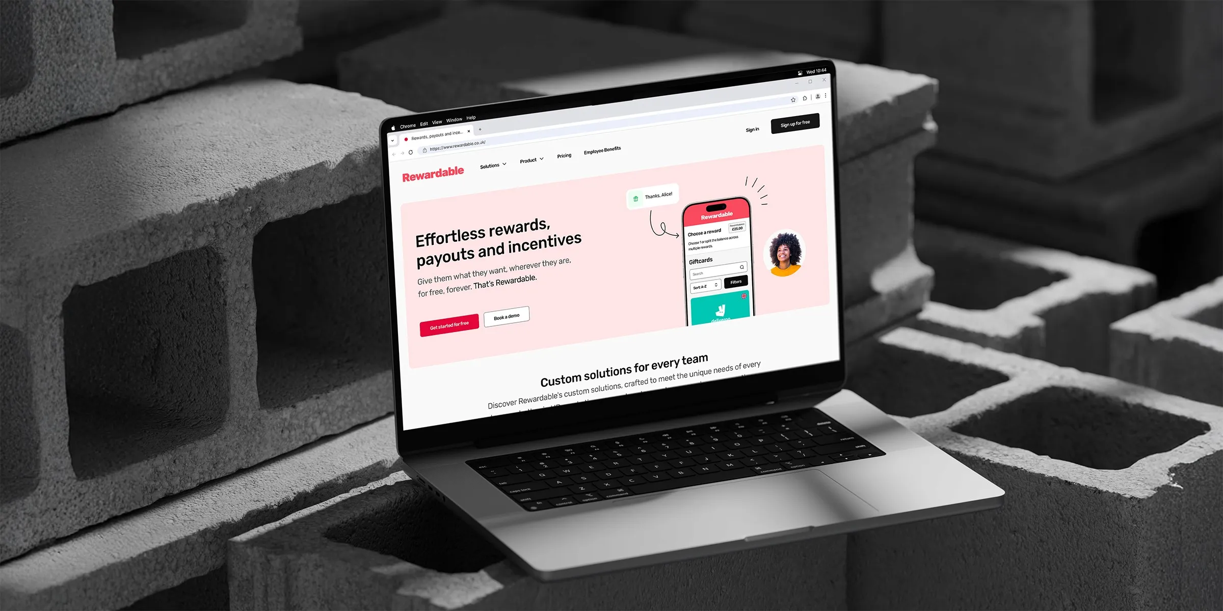 A sleek laptop displaying Rewardable’s website about rewards, payouts, and incentives, set against a backdrop of concrete blocks, highlighting a digital e-commerce platform for gifting.